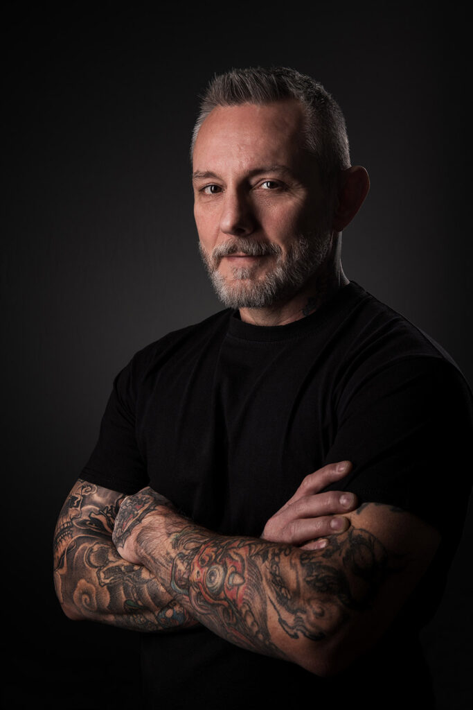 tattoo artist studio portrait looking straight to the camera with crossing arms full of tattoos